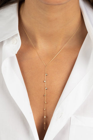 Close-up of a person wearing a white button-up shirt with an elegant, long 14K gold Solid Puffy Hearts Lariat Necklace by Adina Eden, featuring small, evenly spaced gold beads. The shirt's collar is open to showcase the necklace, which has an extender for adjustable drop length, creating a stylish and minimalist look.