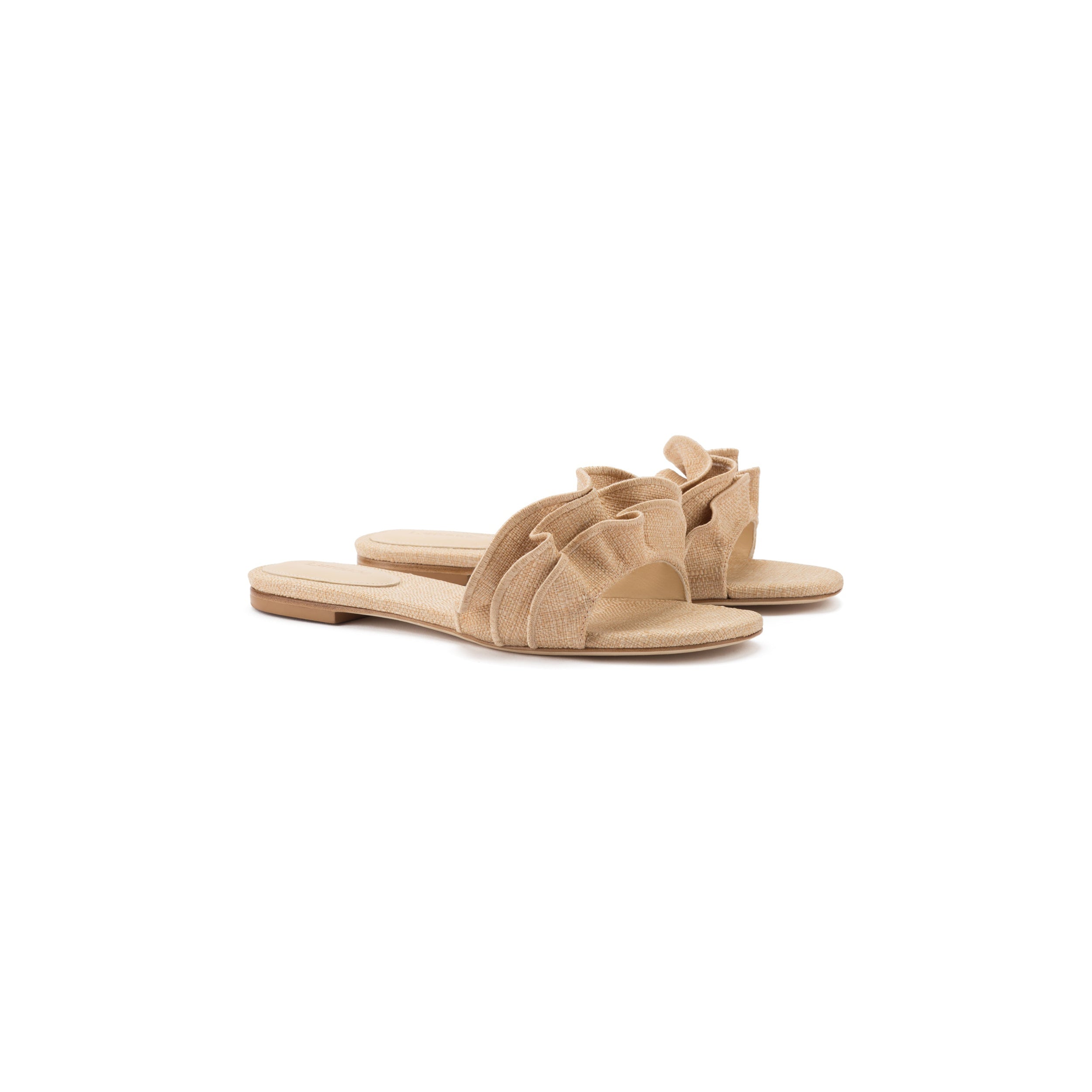 The Ivy Ruffle Flat Mule in Beige Raffia is a pair of flat sandals featuring fabric bow details on the straps, set against a white background. With their casual, summery design and open toes, these bestselling slides boast a simple sole ideal for warm days.