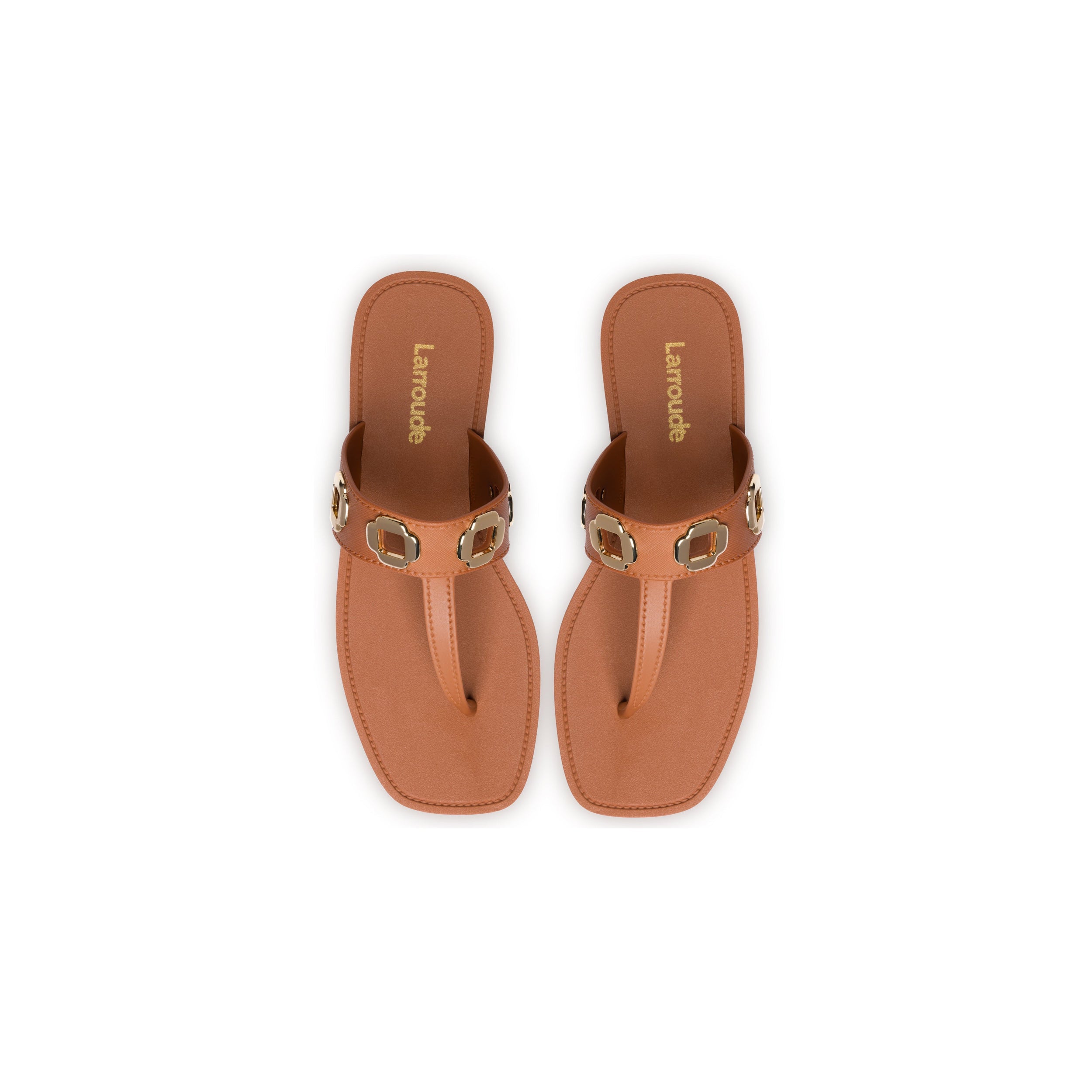 Top view of a pair of Milan S In Caramel PVC sandals with a single wide strap adorned with square gold accents. Featuring a flat sole, these classic silhouette sandals are branded "Lamoude" in gold lettering on the insole. The background is white.