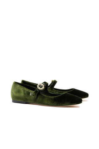 The Blair Ballet Flat In Bosco Velvet is a pair of green velvet Mary Jane ballet flats featuring adjustable ankle fastening and adorned with a flower-shaped, jeweled brooch on each strap. These shoes include a low heel and boast a sophisticated design that combines elegance with comfort, along with memory foam cushion insoles.