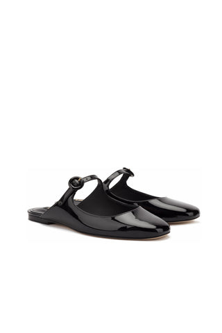 The Blair Flat Mule in Black Patent Leather features a pair of shiny black patent leather slingback flats with a rounded toe, low heel, and adjustable ankle strap with a small buckle. Positioned diagonally on a white background, these stylish shoes resemble mary janes with their classic design.