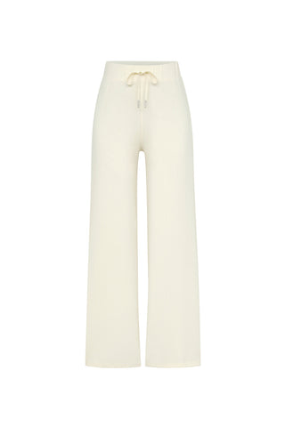 The Daphne Pant - Pearl from Noli Yoga is a pair of off-white, high-waisted, wide-leg pants featuring an elastic waistband and adjustable drawstring. Made from a lightweight modal blend fabric, these pants offer luxurious comfort perfect for casual wear. Ideal for travel, these minimalist pants have no visible pockets or additional details.