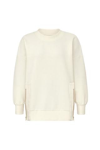 The Isabel Ribbed Pullover - Pearl by Noli Yoga is an off-white, long-sleeve crewneck sweatshirt with ribbed cuffs and two gold zippers near the hem on either side.