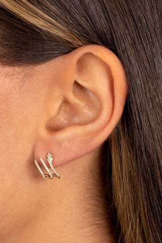 Close-up image of a woman's ear adorned with the Diamond Pavé Snake Cage Stud Earring 14K by By Adina Eden, featuring three parallel bars and a delicate curve, all studded with tiny, natural diamonds. She has long, straight brown hair with a subtle blend of lighter highlights.