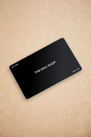 A black rectangular Gift Card, featuring "THE NOLI SHOP" prominently in its center, makes an ideal choice for any occasion. Boasting a sleek matte finish, it sits elegantly on a textured light beige surface, ready to provide checkout redemption instructions.