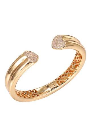 The Pave Heart Open Claw Bangle Bracelet by Adina Eden is a stunning gold bangle with an open design, featuring intricate inner patterns. Both ends of this 18K gold plated brass bracelet are adorned with heart-shaped tips encrusted with small, sparkling clear CZ stones.