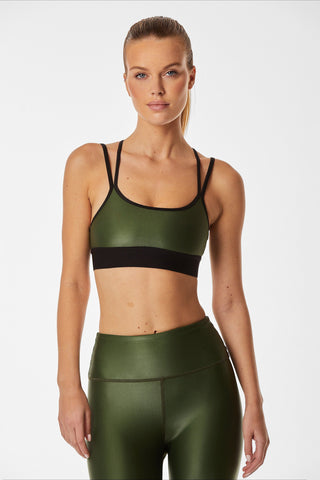 A person with long hair stands confidently in green athletic wear, including the Liquid Jolie Bra in Hunter and moisture-wicking leggings, against a plain white background.