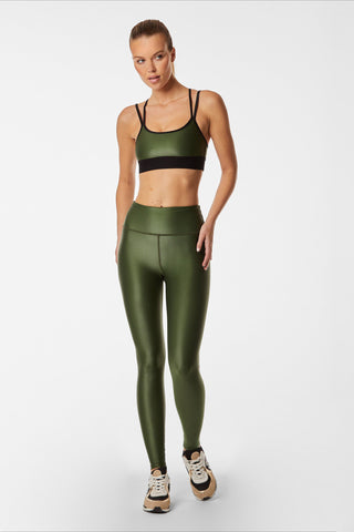 A person wearing a Liquid Jolie Bra - Hunter and a coordinating set of leggings, made from moisture-wicking Liquid fabric, stands against a plain white background. They are dressed in sneakers with their hair pulled back, casually posing in the sleek ensemble.