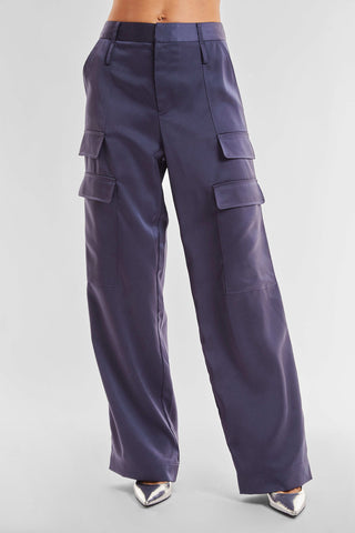 A person wearing the versatile Milan Satin Cargo Pant in navy blue, featuring wide legs and multiple pockets. The pants are paired with pointed metallic silver shoes against a plain, light-colored background.