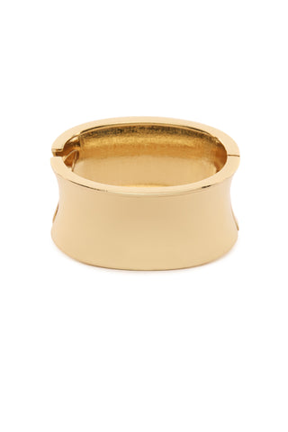 The Monica Bracelet - Gold presents a bold look with its shiny, wide gold metal design that features a smooth, reflective surface and slightly flared edges, elegantly standing upright against a plain white background.