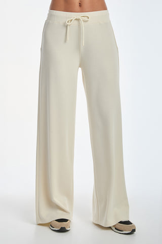 Against a white background, a person wears the luxurious Daphne Pant in Pearl, featuring wide legs and a drawstring waist. Their feet, partly visible, sport black, tan, and white sneakers.