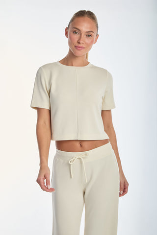 A person with pulled-back hair models the Daphne Soft T-Shirt in Pearl and matching pants, crafted from ultra-soft fabric. They pose against a plain white background, smiling softly. This comfortable, casual outfit is truly a must-have staple.