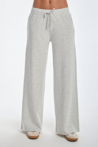 The person is wearing the Daphne Pant in Heather Grey, wide-leg sweatpants made from a soft modal blend with an adjustable waistband and side pockets, effortlessly paired with beige sneakers against a white backdrop.