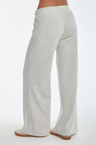 A person is seen from the back wearing the Daphne Pant - Heather Grey, featuring wide legs and made from a soft modal blend, paired with beige sneakers. The plain white backdrop enhances an aura of luxurious comfort.