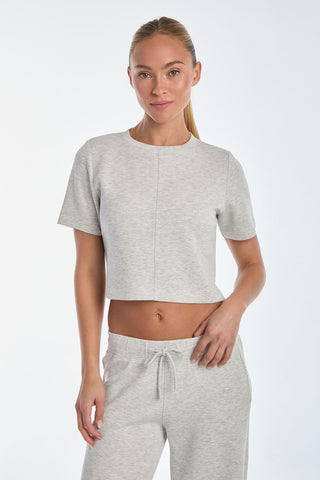 Wearing a Daphne Soft T-Shirt in heather grey with matching drawstring pants, someone stands against a white background. Their long hair is styled in a ponytail, and they gaze at the camera with a neutral expression.