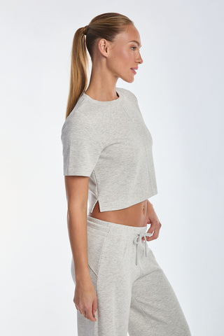 Wearing a Heather Grey Daphne Soft T-Shirt in ultra-soft heathered modal fabric with matching drawstring pants, the person stands in profile, showcasing their style with long hair tied back in a high ponytail against a plain background.