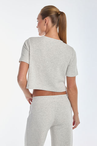 Seen from the back, a person with long hair in a ponytail wears the Daphne Soft T-Shirt in heather grey and matching sweatpants, crafted from ultra-soft modal fabric, against a plain background.