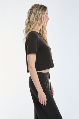 A person with long, wavy blonde hair stands in profile against a plain background, wearing the Daphne Soft T-Shirt - Black with matching pants. This comfortable and casual set is made from lightweight, breathable modal, making it a must-have staple.