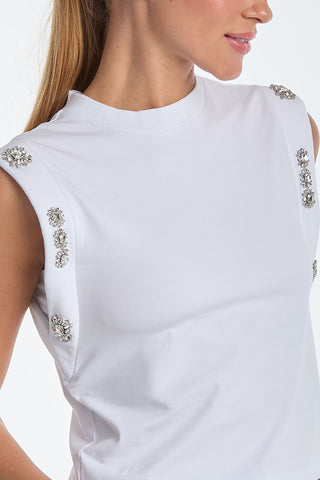 A person wears a sleeveless Dylan Crystal Top in white featuring decorative embellishments on the shoulders, with its chic design highlighted against a plain background.