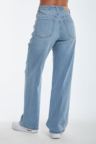 A person is seen from the rear wearing Ivanka Crystal Jean - Medium Blue, high-waisted wide-leg style with white sneakers. The jeans feature two back pockets, visible stitching, and exude subtle elegance against a plain white background.