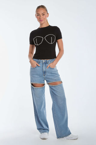 A person is wearing the Rya Crystal T-Shirt in black, featuring a circular bustier design, paired with light blue jeans with thigh cut-outs fastened by a chain. They're standing with hands in pockets and wearing white sneakers against a plain background.