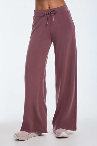 Wearing the Daphne Pant - Orchid, with a drawstring waist and crafted from a soft modal blend, paired with white sneakers, this outfit exudes luxurious comfort against a plain white background.