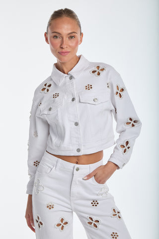 A person models the Kaia Pearl Jean Jacket - White with embroidered pants against a plain background. The buttoned-up, statement jacket complements their slight smile and perfectly pulled-back hair.