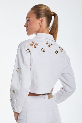 A person with a ponytail is wearing the Kaia Pearl Jean Jacket - White, adorned with beaded floral embroidery and intricate cut-out designs on the back and sleeves, paired with white pants against a plain white background.