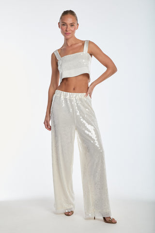 A woman poses confidently in a statement look, wearing the Alba Sequin Pant in Pearl and a matching crop top. The wide-leg silhouette pairs with her open-toed shoes as she stands against a plain white background with one hand on her hip.