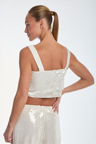 Wearing the Zoey Sequin Crop Top - Pearl, a person with a ponytail and matching pants faces backward on a plain white background, hand on hip, highlighting the sparkling sequin design.