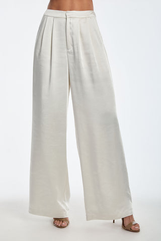 A person is wearing the Valentina Satin Pant in Pearl, high-waisted and wide-leg, with tan high heels. The silky material adds a satiny soft touch. The image focuses on the lower half against a plain background.