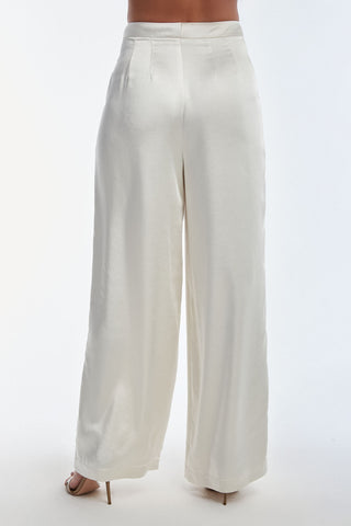 A person elegantly stands on their toes, wearing the Valentina Satin Pant - Pearl. These high-waisted, wide-leg satin pants feature subtle pleats at the waist and showcase smooth, flowing fabric from a graceful back view.