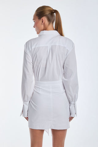 A woman with long hair in a ponytail is wearing the Lana Wrap Dress - White, an elegant poplin shirt dress. She is facing away, showcasing its long sleeves and belt against a plain white background.