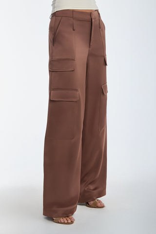 A person wears the Milan Satin Cargo Pant in Mocha, featuring wide legs and side cargo pockets. They are styled with a light top and open-toed heels against a plain white background.