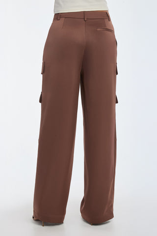 A person is seen from the back wearing the Milan Satin Cargo Pant in Mocha, featuring a wide-leg silhouette and multiple pockets. Paired with a tucked-in white shirt, they stand against a plain light-colored background.