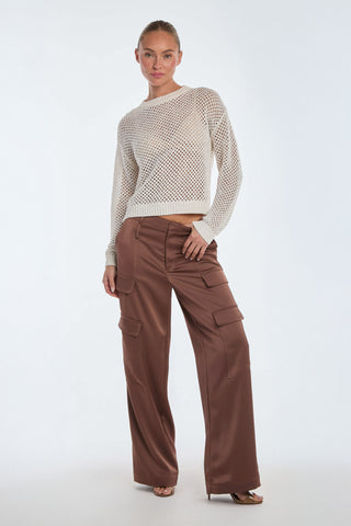 A person stands against a white background, wearing a sheer white knit sweater and the Milan Satin Cargo Pant in Mocha, showcasing distinct cargo details. They have one hand slightly tucked in a pocket and exude confidence with their neutral expression.