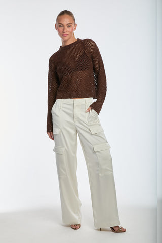 Posing against a plain background, a person exudes chic style in the Lucie Knit Sequin Sweater in Espresso and cream cargo pants, with their hair neatly tied back and one hand in a pocket.