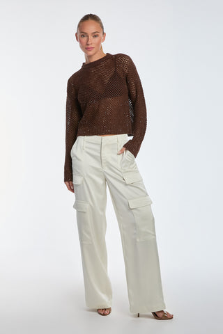 A person stands against a plain background wearing the Lucie Sequin Crochet Top in Espresso and white cargo-style pants. One hand is in their pocket, and they look directly at the camera, exuding a casual yet glamorous style.