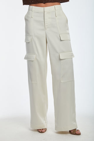 A person in off-white Milan Satin Cargo Pant - Pearl, mid-rise wide-leg style with multiple pockets. They're paired with open-toed shoes and a brown top, but only the lower half is visible.