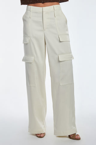 A person in Milan Satin Cargo Pant - Pearl, featuring high-waisted, wide-leg design crafted from silky satin fabric, stands against a plain background. They pair it with open-toed sandals and a dark top.