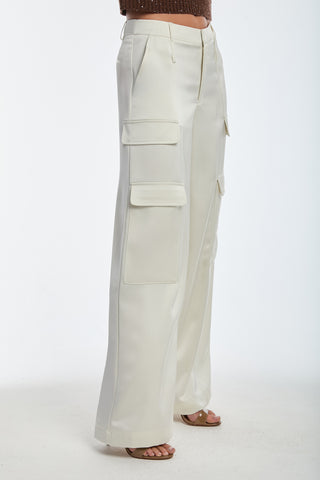 A person wears the Milan Satin Cargo Pant in pearl, featuring a wide-legged and mid-rise design with multiple large utility pockets. The slightly flared pants are worn with brown open-toed heels against a plain white background.