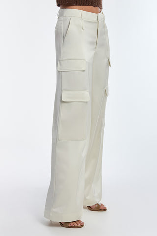 A person is wearing Milan Satin Cargo Pants in pearl, featuring versatile wide-leg design and multiple pockets, paired with beige sandals. The background is a plain, light color.