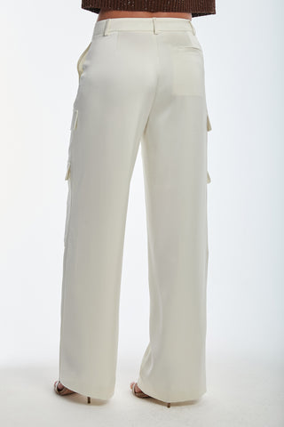 A person models the Milan Satin Cargo Pant in Pearl, featuring high-waisted, wide-leg design with side pockets and subtle cargo detail. The elegant silky satin fabric complements the pants' belt loops as they pose against a plain background, revealing only the back view.