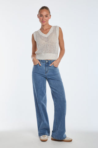 A person stands confidently against a white background, wearing the chic, sleeveless Addison Sequin Knit Top - Pearl paired with high-waisted, wide-leg jeans. Hands are casually in their pockets, completing the look with white sneakers.