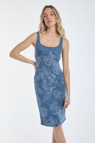 A woman confidently poses in the Flora Rose Denim Dress - Medium Blue, featuring a blue floral pattern and corset details. Her long blonde hair is styled in loose waves, elegantly complementing the fitted, sleeveless dress with a scoop neckline against a plain white background.