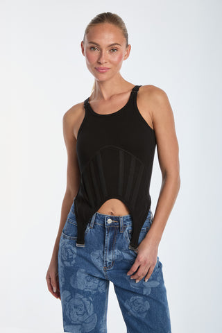 A person with hair pulled back is wearing a black Kiara Garter Tank Top, featuring corset-inspired buckle details, and blue jeans with floral patterns. They are smiling against a plain white background.