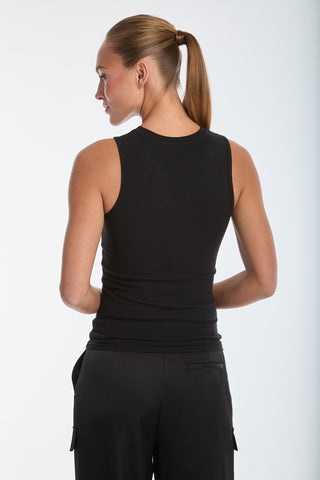 A woman with long hair in a ponytail wears a black Rosette Tank Top and black pants. She stands with her back to the camera, slightly turned to the side, against a plain white background.