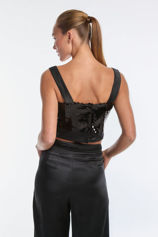 A woman with long hair in a ponytail is shown from behind, wearing the Zoey Sequin Crop Top - Black and high-waisted black pants. She stands against a plain white background, radiating elegance and style.