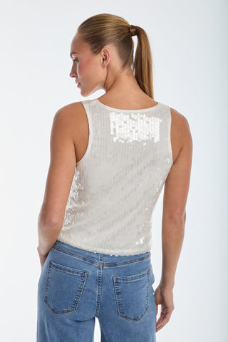 A person with long hair in a ponytail wears a sleeveless Sophia Sequin Tank - Pearl with blue jeans. The shimmering white top dazzles as they stand slightly turned against a plain, light-toned background.