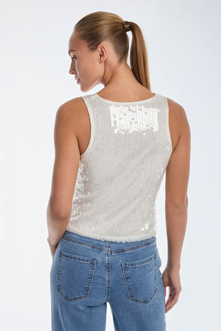 A person with long hair in a ponytail wears a sleeveless Sophia Sequin Tank - Pearl and blue jeans, standing against a plain background. The white top has a sequined texture, and they face away from the camera.